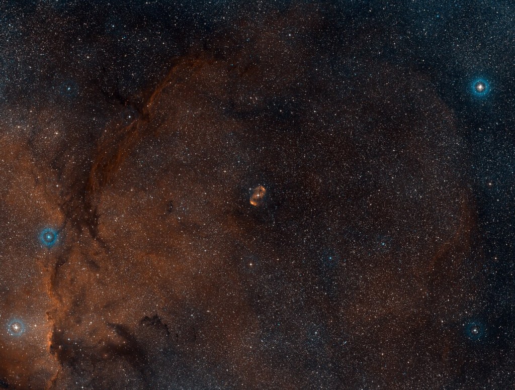 A galaxy in space with stars. The nebular NGC 6164/6165 is show in the middle, with a S-shaped nebula in orange. 