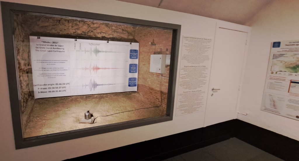 Een glas met daarachter een seismometer en een grote poster