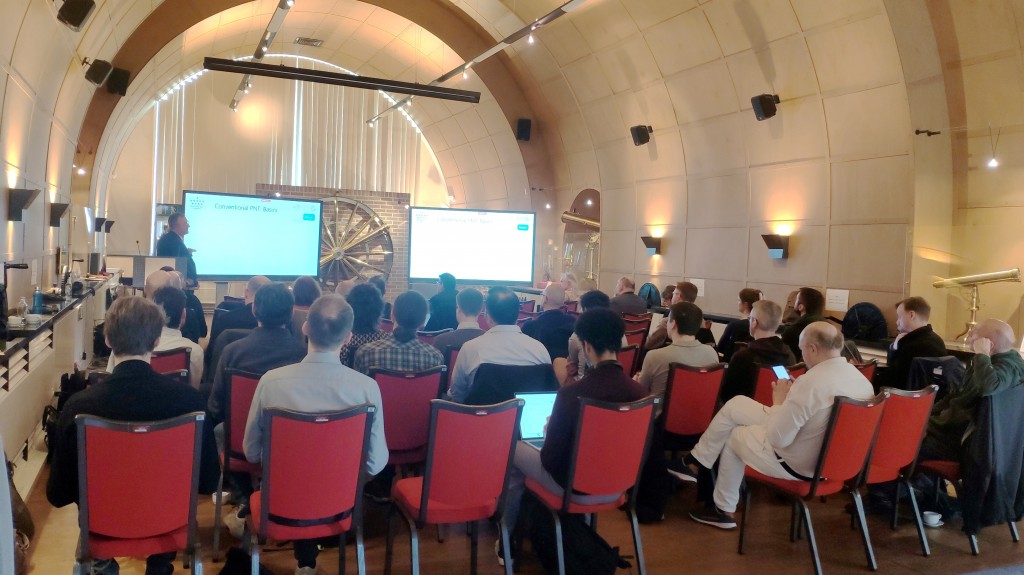 People in a conference room watching two screens while a presenter explains the content